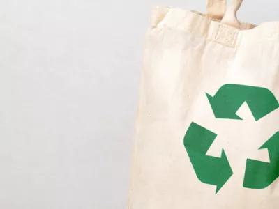 A canvas tote bag with a recycling symbol on the front and with a sleeve of clothing coming out the top of the bag