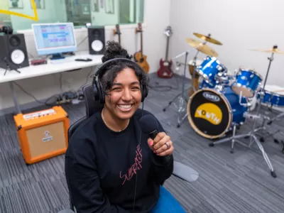 A smiling woman holds a microphone with a drumkit behind her