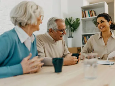two older adults sitting at a table with a younger person who is referencing papers.
