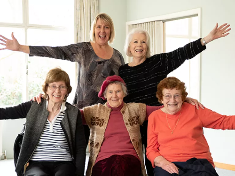 group of 5 older adults smiling with their arms outstretched