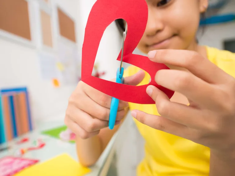 a young girl cuts out a red paper heart
