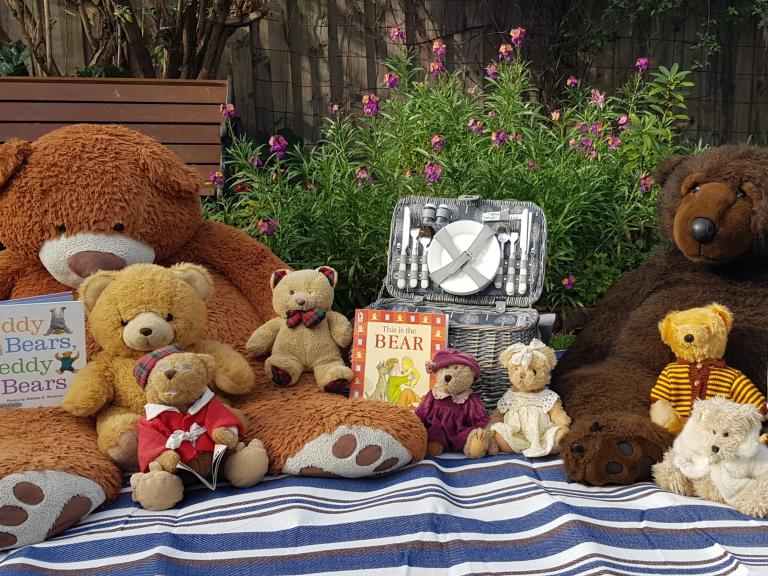 A picnic blanket covered with seated teddy bears, a picnic basket, and children's books
