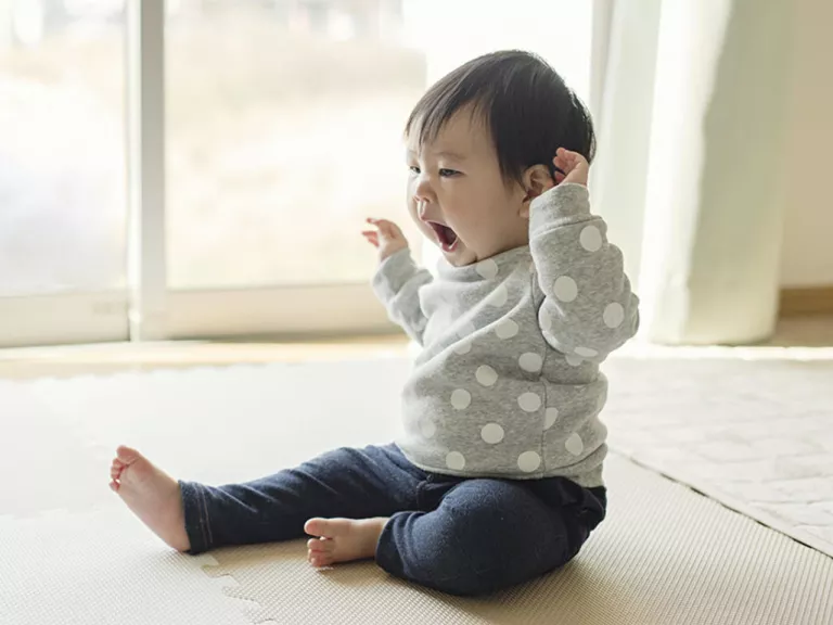An older baby is sitting up and yawning