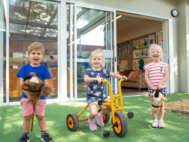 Three young children laughing in an outdoor kindergarten setting