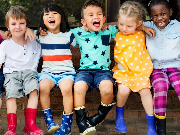 5 children sitting on a ledge with their arms around each other, smiling.