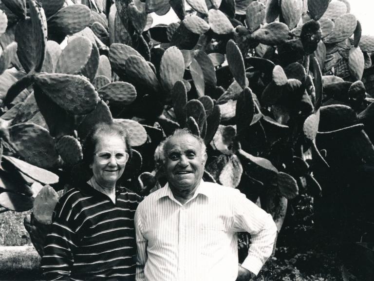 Twp people standing in front of a large prickly pear cactus. They are smiling at the camera.