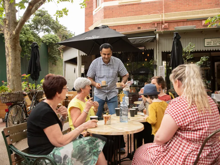 Man serving coffee to an outdoor table at a cafe.