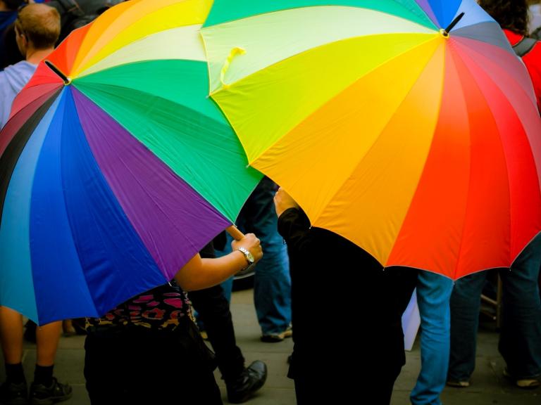 Two people holding rainbow umbrellas that cover them