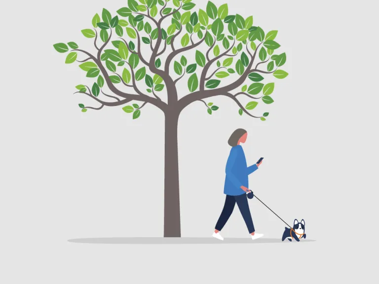 A person walking a small dog while using their phone and standing under a tree