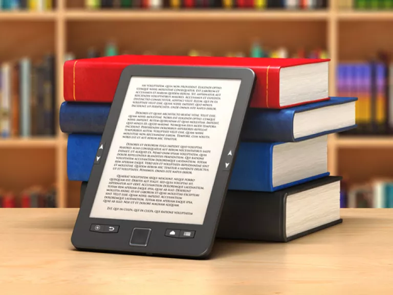 an ebook reader leans against a pile of hardcover books