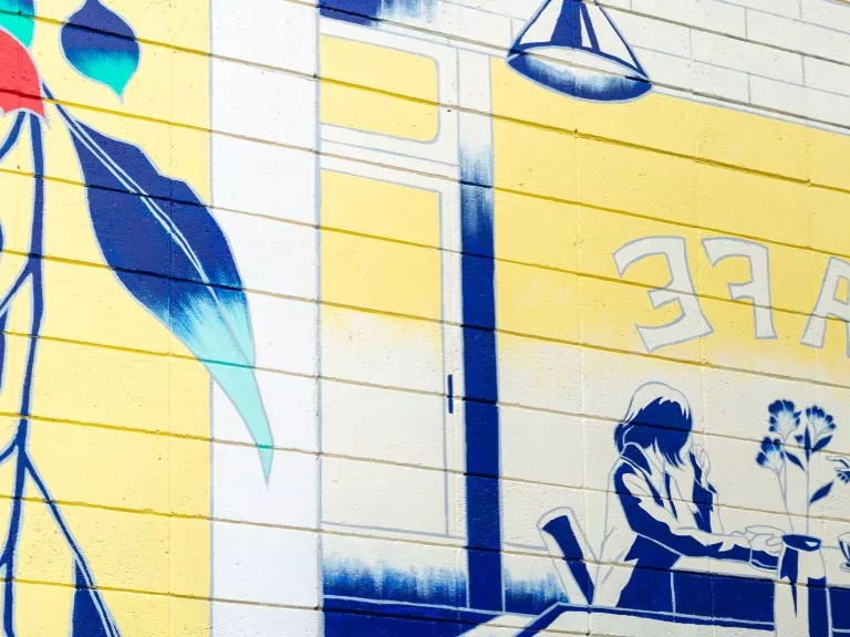 a mural on a white wall shows a couple sitting at a cafe framed by eucalypt flowers