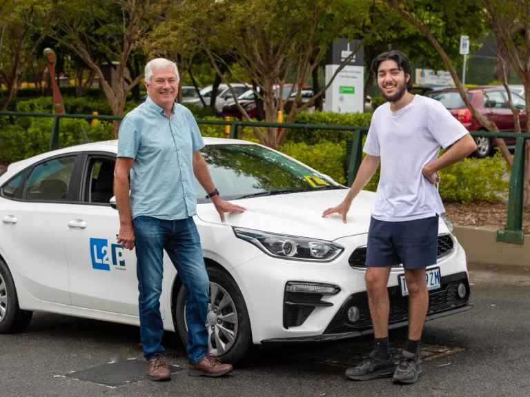 An older man and a younger man stand proudly next to a white car