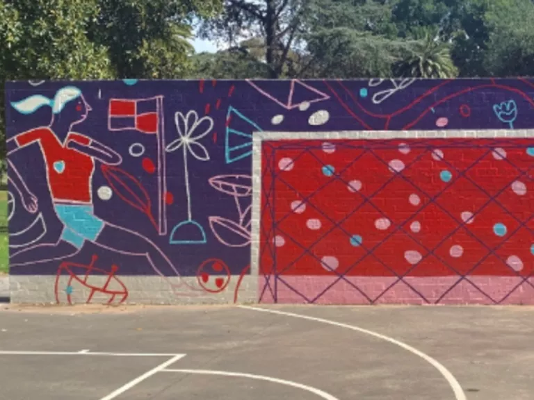 A mural on a wall in a park showing two soccer players moving toward a goal in bright blue and red colours