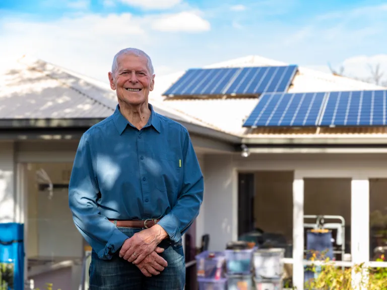 An older person standing outside a residential home which has solar panels on the roof