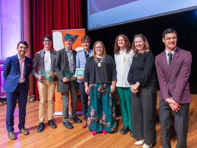 A group of young people standing with the Mayor, holding their winners plaques