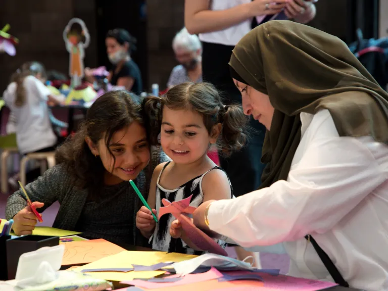 An adult and 2 children cutting paper and colouring