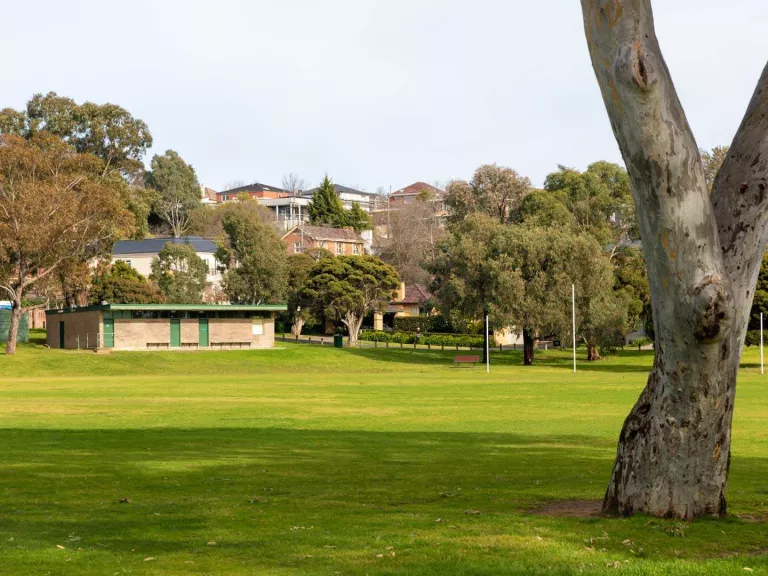 A view across a green sportsfield looking towards a brick building. 