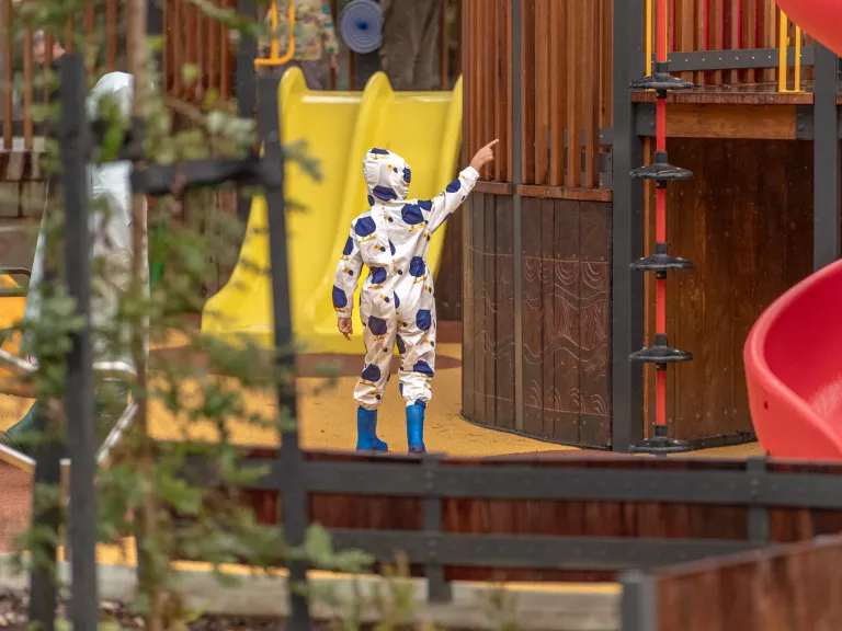 child in gumboots and raincoat pointing up at the playground