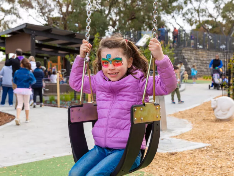 a child with colourful face paint is on the swings at a playground
