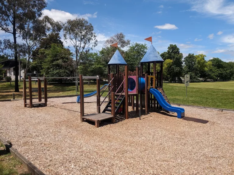 a small playground with chip bark, slide and climbing tower
