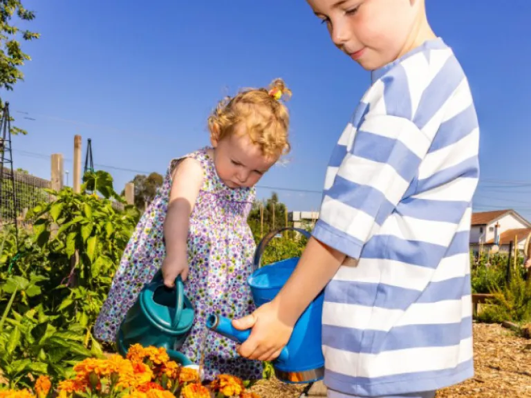 Two children water plants in community garden