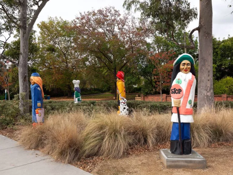 four colourful figures and a dalmatian carved from wood. The figures are in a grassy park. The figure in the foreground holds a stop sign
