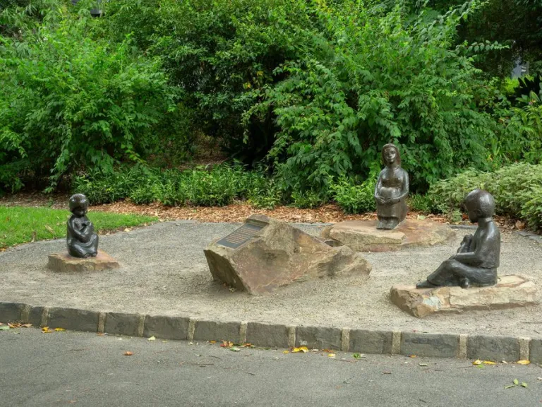 Three bronze figures of children positioned around a central plaque. Green leaves make up the backdrop