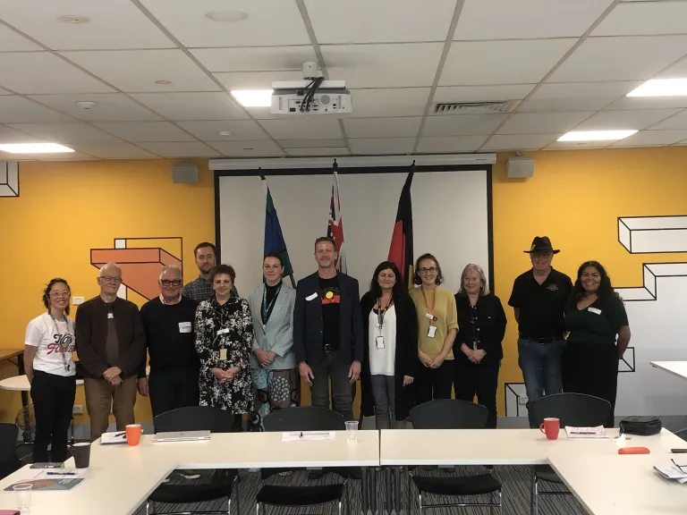 group of 12 people standing together in a meeting room in front of the Australian, Aboriginal, and Torres Strait Island flags