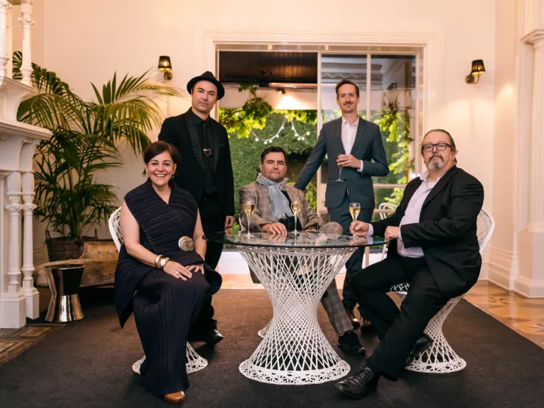 5 well-dressed adults sit at a wicker dinner setting