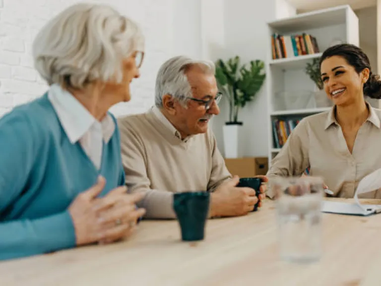 two older adults sitting at a table with a younger person who is referencing papers.