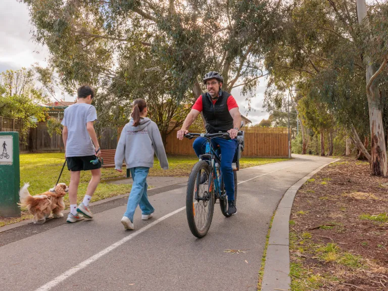 A man rides a bike on a shared footpath. A man and woman walk their dog on the same footpath.