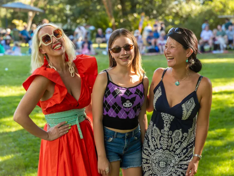 Three women pose for a photo in a sunny park.