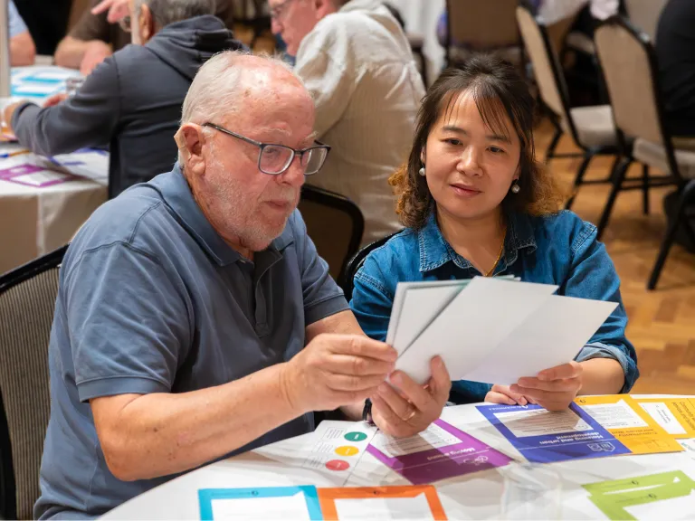A man and a woman are in a community consultation workshop, they both read materials supplied at the workshop.