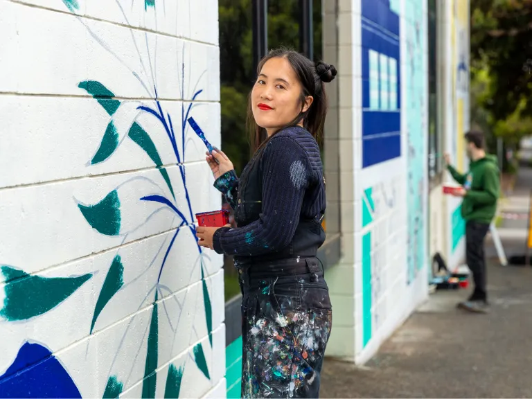 A young woman paints a mural on a community wall.
