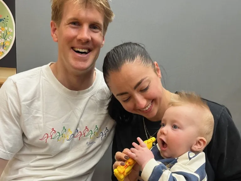 2 people with a baby smiling at the camera