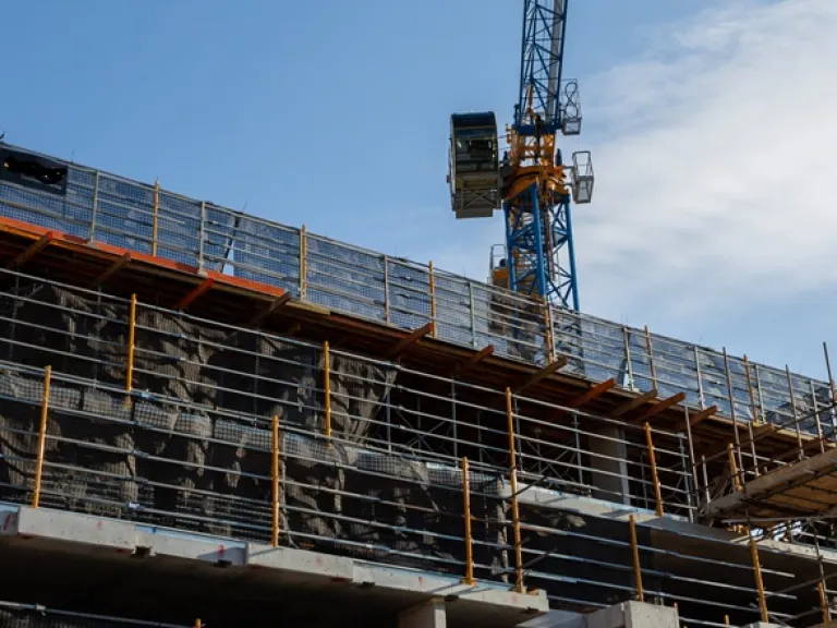 A building in construction surrounded by scaffolding. In the background a crane is partially visible.
