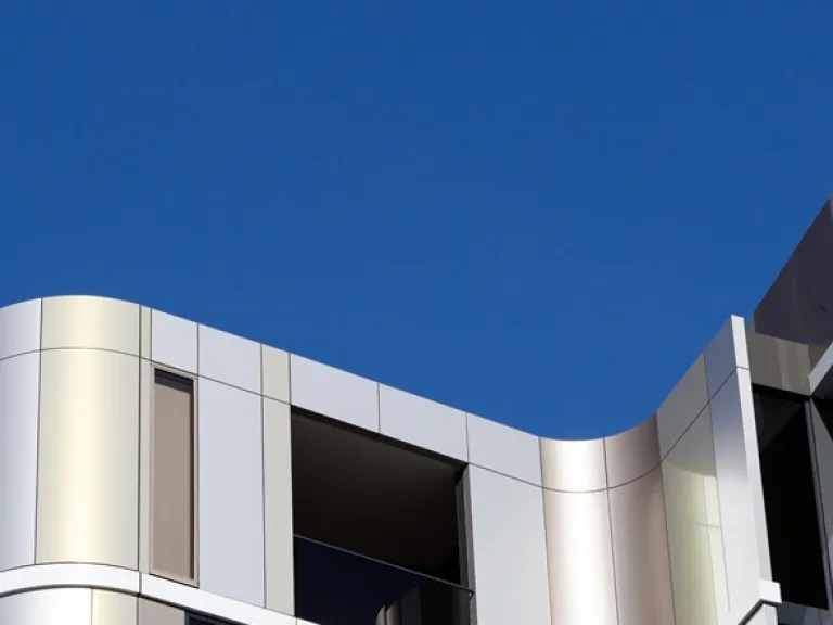 Looking up at a grey building with curved corners against a bright blue sky.