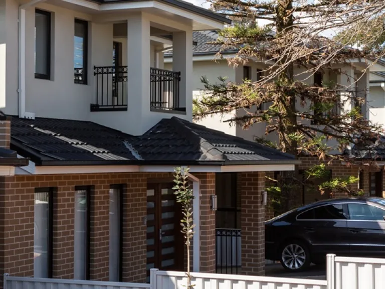 A row of brick and rendered townhouses. Each has a low fence separating the front yards.