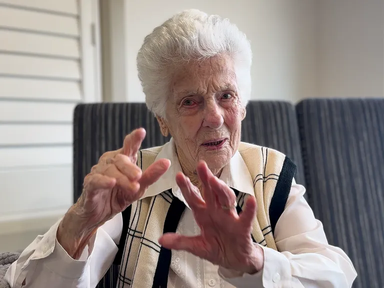 Woman with short white hair speaking expressively with her hands.