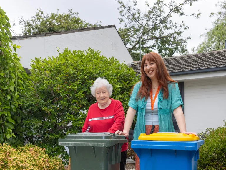 Two people standing behind a general waste and a recycling bin.
