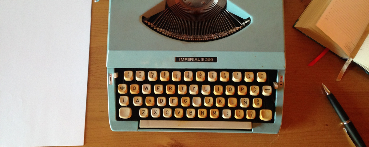 a typewriter with a blank page inserted sits on a desk