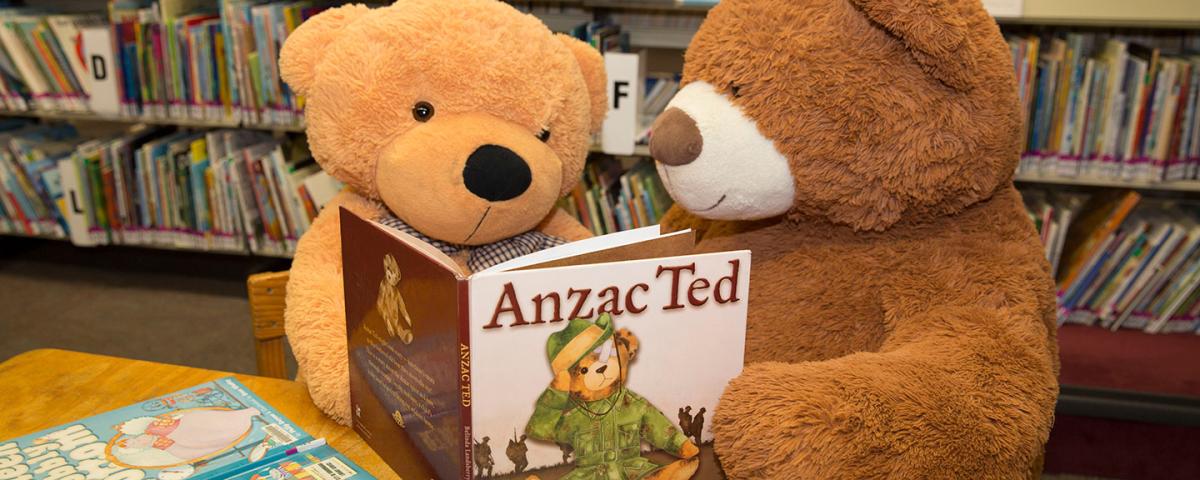 Two people dressed as teddy bears read a book in the library