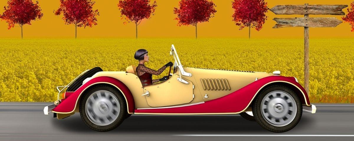 Image named Aussie Deco featuring woman in a vintage sports car driving by a yellow field with red leaf trees in the background.
