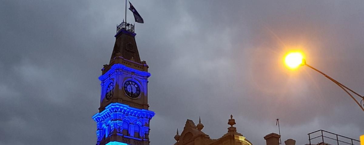 Clock tower with blue lights and grey clouds in the background. 