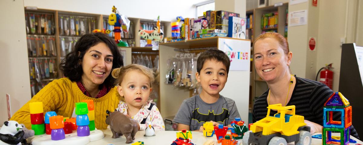 Two women sit with two kids at a table at a toy library