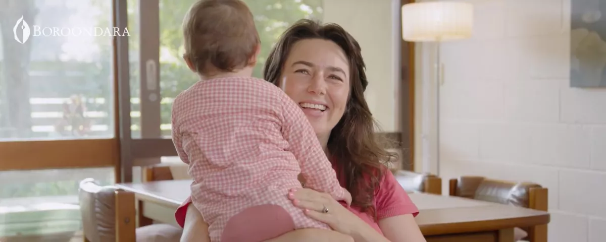 a smiling woman hugs a baby wearing a onesie jumpsuit
