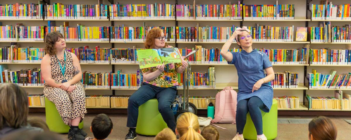 3 people in a library read a picture book and use sign language to an audience