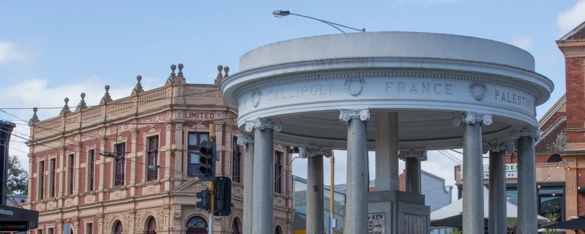 Street view of a cenotaph building on the edge of a roundabout with a historic building in background