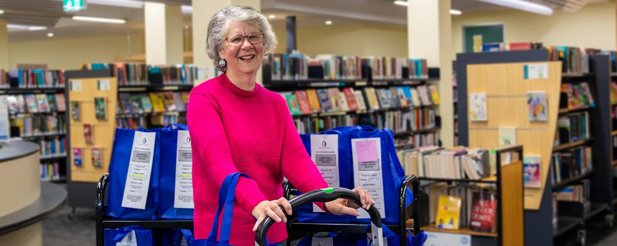 Volunteer Elizabeth Smith pushing trolley among library shelves.