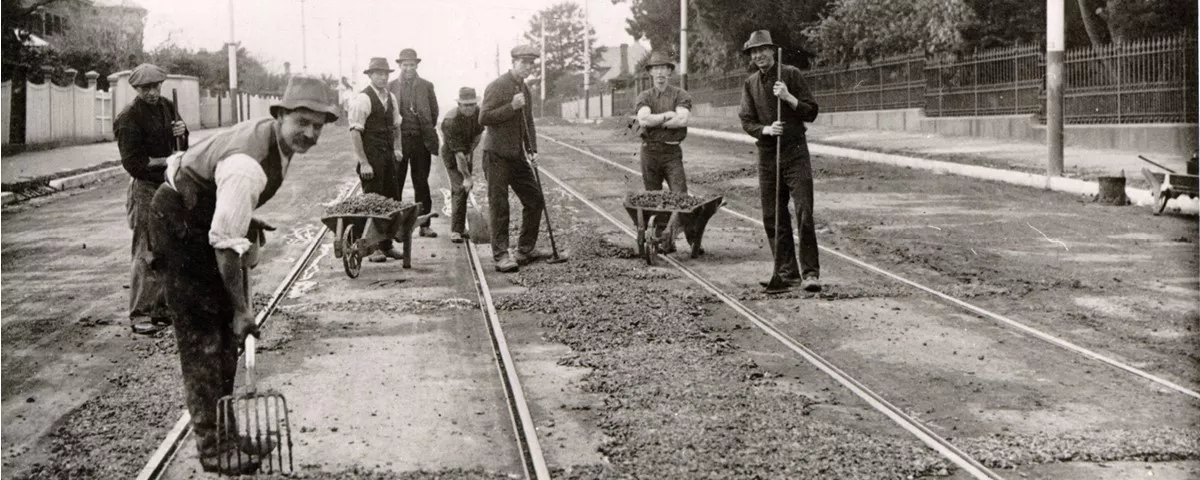 Historical black and white photo of workers with wheelbarrows and pitchforks repairing Riversdale Road